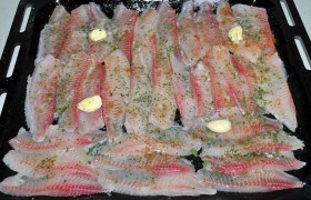 Сбрызгиваем лимонным соком, посыпаем кориандром, травами, петрушкой, перцем и солью. Сливочное масло растапливаем и поливаем рыбу. Выкладываем раздавленные дольки чеснока.