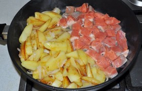 жарим 2-3 минуты, распускаем сливочное масло и выкладываем кубики рыбы. Можно смешать с картошкой, но лучше получается, если мы освобождаем для рыбы часть сковороды. Продолжаем жарить, посолив картофель, перемешивая и переворачивая и его, и рыбу, 3-4 минуты.