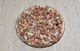 Кусочки филе селедки мелко нарезаем, смешиваем с шинкованным луком и выкладываем первым слоем. 