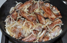 Засыпаем к мясу полукольца лука и нарезанный чеснок, меняем огонь на тот, что ближе к среднему, помешивая и переворачивая, продолжаем жарку ребрышек с луком 8-9 минут.