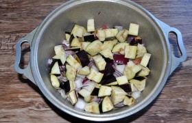 На мясо выкладываем крупно шинкованный лук, на него - слой кубиков баклажана,