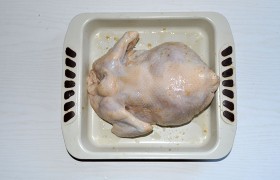 Включив духовку на подогрев до 180°, промазываем растительным маслом форму. Ножки связываем, а крылышки заправляем в маленькие надрезы-кармашки на коже по бокам. Кусочки яблока, петрушку, сельдерей заталкиваем внутрь – они придадут аромат и дополнительную сочность курице. Кладем грудкой вниз, поливаем маринадом из пакета.