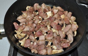 Засыпаем шампиньоны и продолжаем обжаривать вместе с мясом еще 1,5-2 минуты.  Этого достаточно, чтобы мясные кусочки стали светлыми и начали появляться корочки, т.е. они фактически уже готовы.