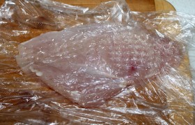 Поочередно помещая куриные филе в пищевой пакетик, деревянным молотком отбиваем их, особенно толстую часть, чтобы они стали более ровными по толщине.