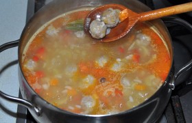 Часть нашинкованного нами лука мы сразу положили в мясной фарш, посолили его, поперчили и отбили, сформовали маленькие, по 20-25 мм, фрикадельки. И теперь, когда картошка почти готова, кладем фрикадельки в кастрюлю, а следом закладываем заправку, бросаем горошки перца, лавровый лист, солим.