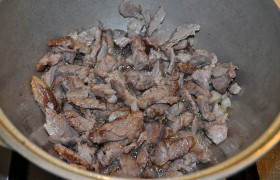 В раскаленный на сильном огне жир выкладываем мясо, перемешивая, обжариваем его.