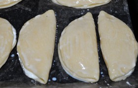 Края слегка прижимаем. Заделывать или нет край - дело вкуса. Кому-то нравятся закрытые сочни, кто-то любит, чтобы часть творога была видна. Выкладываем сочни на противень, застеленный бумагой или ковриком для выпечки, смазываем их слегка взбитым желтком и отправляем в духовку, нагретую до 200°, где они пекутся обычно 15-20 минут.