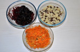 Салат мы готовим слоеный, а потому очищенные картофелины пропускаем через крупную терку и соединяем с изюмом, замоченным на 5 минут в кипятке и обсушенным. Корейскую морковку перемешиваем с дроблеными грецкими орехами. А крупно тертую свеклу – с нарезанным черносливом.