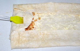 Подворачиваем  поперечный, затем правый и левый длинные края лаваша и начинаем скатывать рулет. После каждого поворота смазываем лаваш яйцом. Завернув, смазываем верхнюю часть.