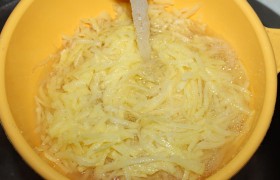 Очищенный картофель крупно натираем и минуту-полторы промываем струей воды в дуршлаге (меньше станет крахмала). Ждем, когда воды не останется вовсе, потряхивая дуршлаг и прижимая картошку.