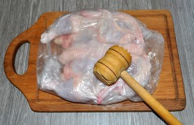 Тушку цыпленка кладем в прозрачный пакет из пищевой пленки и отбиваем кухонным молотком, избавляясь тем самым от брызг и повреждения кожи цыпленка. Отбивать надо как следует, больше всего – боковой поверхностью молотка, чтобы распластанная тушка стала плоской. Мужчины способны делать это кулаками.