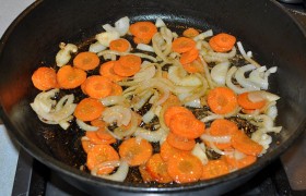 Выложив мясо в тарелку, в сковороду кладем лук и морковь. Все так же перемешивая, жарим 2 минуты.