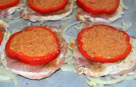 Противень выстилаем пергаментом или фольгой, засыпаем луком, с которым мариновалось мясо. Раскладываем отбивные, на каждую кладем кружок сладкого перца, который заполняем подготовленным пюре.