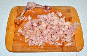 С копченого куриного окорочка снимаем кожу, мясо отделяем от костей и нарезаем мелкими кусочками.