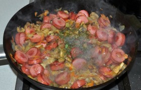 Соединяем в одной сковороде овощи с сардельками и грибами, тушим 3-5 минут, посыпаем зеленью, накрываем и выключаем рагу.