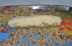 Орехи измельчаем (не сильно) в пакете с помощью скалки, высыпаем на плоскую поверхность. Каждую колбаску катаем по орехам, немного прижимая, чтобы орехи вдавливались и держались на тесте.