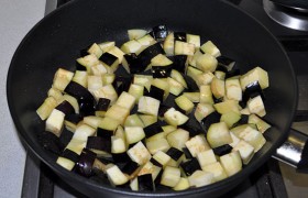 На другую конфорку ставим вторую сковороду. Пока нагревается масло, нарезаем баклажан на небольшие кубики и обжариваем, помешивая и переворачивания, 4-5 минут на сильном огне.