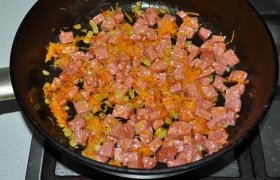 А в сковороду с овощами добавляем мелкие кусочки нарезанной колбасы. Обжариваем 3-4 минуты. 