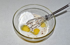 Для заливки соединяем в миске крахмал, молоко и яйца, посыпаем перцем и солью по вкусу, вымешиваем венчиком или обычной вилкой.